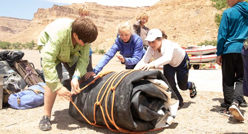 A group of people work together to roll up a large tarp. 